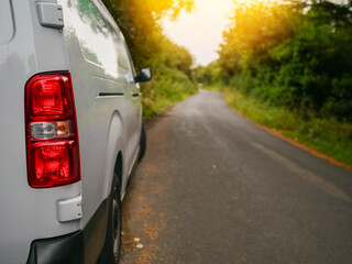 Wall Mural - A white medium size van is parked on a small county road in rural area with a red tail light. The road is empty and the sun is shining brightly. Product delivery to remote locations concept.