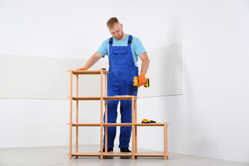 Poster - Worker with electric screwdriver assembling wooden shelving unit indoors