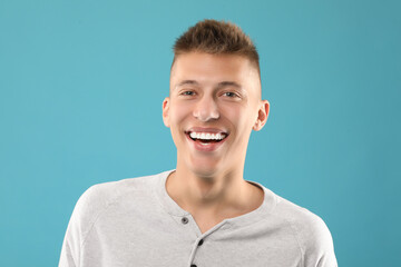 Canvas Print - Happy young man on light blue background. Dental veneers