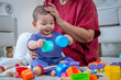 © SKW - A woman and a baby are playing with toys on a carpet.