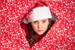 © ADDICTIVE STOCK - Young girl in Santa hat peeks out from red festive wrap