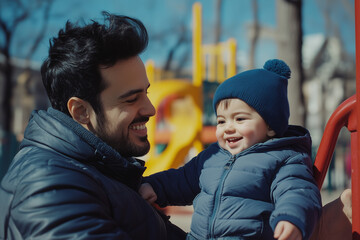 Wall Mural - smiling hispanic father with his son happy toddler wearing blue coat and hat large smile, complicity, on a playground closeup shot of latino american family happiness cheerful fall