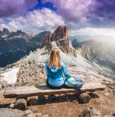 Wall Mural - girl with backpack is sitting on the wooden bench on mountain peak in beautiful alpine mountains at 