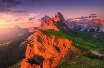 Wall Mural - Seceda mountain at beautiful sunset in summer in Dolomites, Italy. Colorful landscape with red mountain peaks, rocks, alpine meadows, trail, green grass, purple sky with clouds. Hiking in Alps. Nature