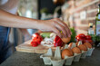 © Geber86 - Woman reaching for an egg from a carton in the kitchen with fresh vegetables in the background