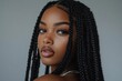 © Mickey - A close-up portrait of a beautiful black woman with long black braids. She has on a soft, natural makeup look with long lashes and lip gloss. The photo is shot from a slightly low angle, giving the vi