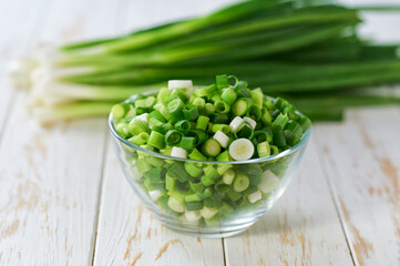 Chopped fresh green onion or scallions in a clear glass bowl , on a light table.