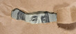© nndanko - A piece of a hundred dollar bill is visible through a hole in the paper. Symbolism of hidden or concealed wealth, money that remains out of sight, or financial resources.
