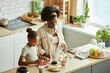 © Seventyfour - High angle shot of African American mother and little daughter preparing fruits for smoothie cooking healthy breakfast together at cozy beige kitchen on large counter, copy space
