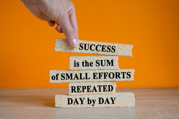 Concept words Success is the Sum of Small Efforts Repeated Day by Day on brick blocks. Beautiful wooden table orange background. Businessman hand.