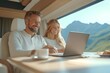 © Pukan - Young couple working inside a sunlit camper van with a laptop, enjoying coffee, with mountains visible through the window.
