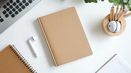 Top view of a blank book with a brown cover, alongside earphones and a wooden pencil in a holder, all placed on a white desk background.