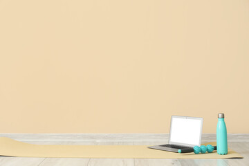 Wall Mural - Laptop with bottle of water and massage roller on fitness mat near beige wall in room