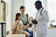 © pressmaster - Engaging with child patient and parent while holding tablet in office. Medical professional smiling, creating comforting environment for young patient, promoting positive interaction