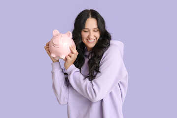 Wall Mural - Pretty young woman with piggy bank on lilac background