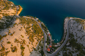 Aerial view of a winding coastal road near the tranquil blue waters of a secluded cove. 