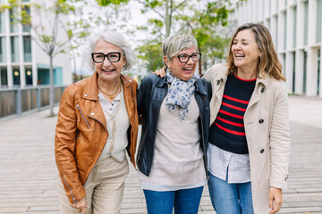 three mature retired women laughing while walking together outside. small group of 60s females havin