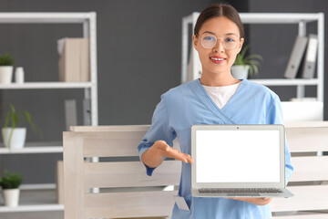 Canvas Print - Young female medical receptionist pointing at modern laptop in hospital