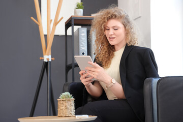 Sticker - Young beautiful businesswoman sitting on armchair and using tablet in office