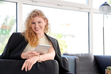 Young beautiful businesswoman sitting on armchair and using tablet in office