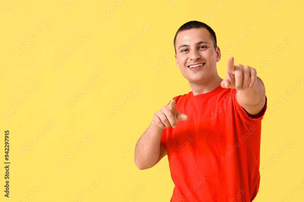 Handsome young happy man pointing at viewer on yellow background
