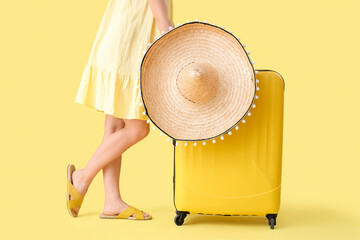 Wall Mural - Young woman with suitcase and sombrero  on yellow background