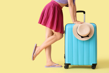 Wall Mural - Young woman with suitcase and hat on yellow background