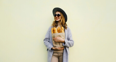 Wall Mural - Beautiful happy smiling young woman holding grocery shopping paper bag with white bread baguette