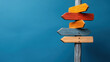 © khonkangrua - Wooden post with vibrant directional signs against a blue background, symbolizing choices, directions, and decision-making.
