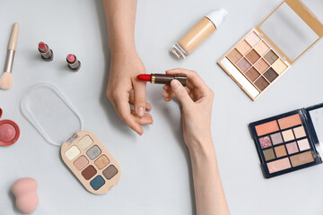 Wall Mural - Female hands with red lipstick and different cosmetic products on grey background, closeup