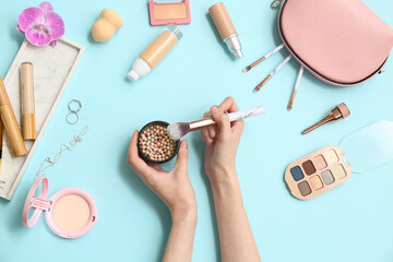 Wall Mural - Female hands with powder pearls, makeup brush and different cosmetics on color background