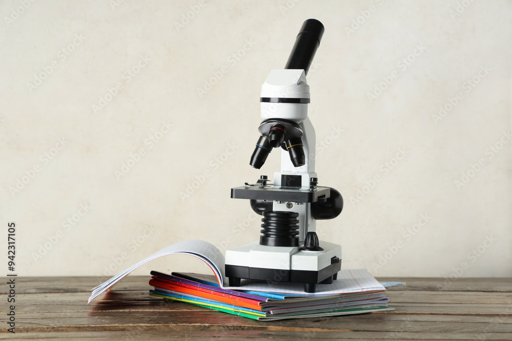 Modern microscope with and copybooks on wooden table against white grunge background