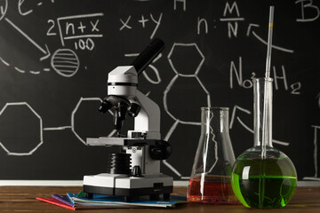 Wall Mural - Modern microscope and flasks on wooden table near chalkboard with chemical formulas