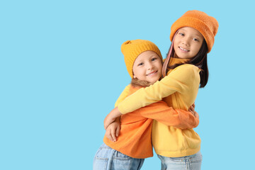 Wall Mural - Cute little happy girls in autumn clothes hugging on blue background