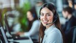 © Thanthara - Smiling female customer service representative wearing a headset working in a modern call center with colleagues in the background.