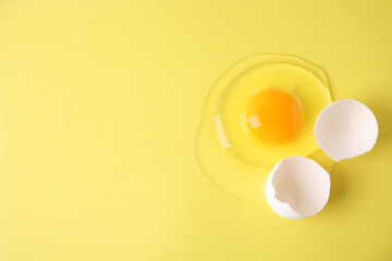 Broken raw egg and shell on yellow background, top view. Space for text