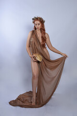 Canvas Print - Full length portrait of beautiful female model wearing silken toga robes with golden crown, historical fantasy greek goddess aphrodite costume, holding seashell skull. Isolated on studio background