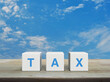 © grapestock - TAX letter on white block cubes on wooden table over blue sky with white clouds, Business and finance concept