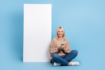 Wall Mural - Full body photo of satisfied retired lady influencer sitting with phone browsing her new interface apple device isolated on blue background