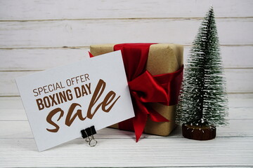 Wall Mural - Boxing day Sale text on paper card with gift box and artification pine tree on wooden background