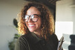 © Flamingo Images - Young businesswoman with a big smile standing in an office. She has a clipboard in her arms, curly hair and wears big black glasses.