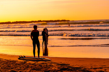 Wall Mural - A man stands on the beach with his surfboard, watching the waves