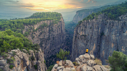 Wall Mural - A man climbing Tazi Canyon and watching the view. The sun is added to the magnificent harmony of trees and mountains in the canyon.