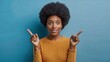 © Tatiana - A pleased dark-skinned woman with an Afro hairstyle, pointing with both forefingers to empty space for your promotion, against a blue background.