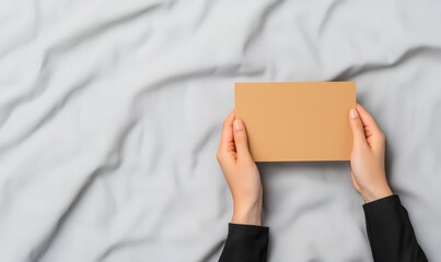 blank brown card mockup held by hands on grey fabric background - minimalist design concept for branding or marketing