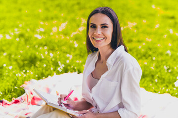 Photo of attractive young cheerful girl sit picnic blanket write notebook wear white garment having fun outside outdoors