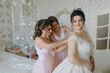 © Vasil - Three women are getting ready for a wedding. One of the women is wearing a white dress and the other two are wearing pink dresses. The bride is smiling and the women are helping her get dressed
