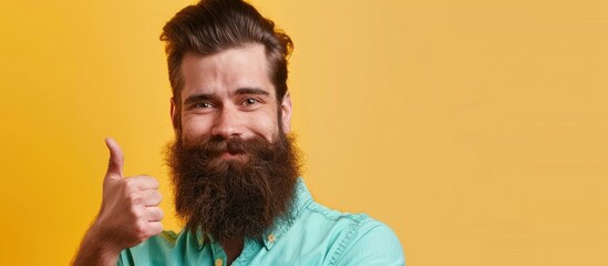 Poster - A charming bearded man wearing a mint shirt gives a thumbs up gesture against a yellow background with copy space image