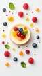 © AURA COLLECTIONS - A single cheesecake with blueberries, raspberries and mint on top, surrounded by scattered blueberries, raspberries, mint, and orange-colored jelly drops on a white background.