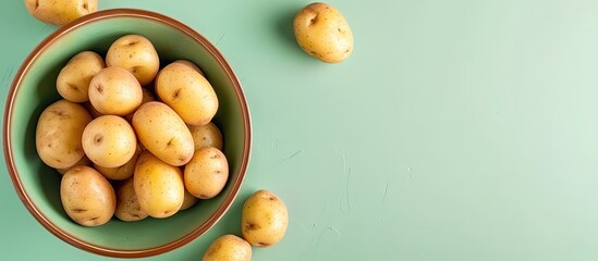Poster - Top view of a bowl filled with fresh raw potatoes on a green background featuring copy space image